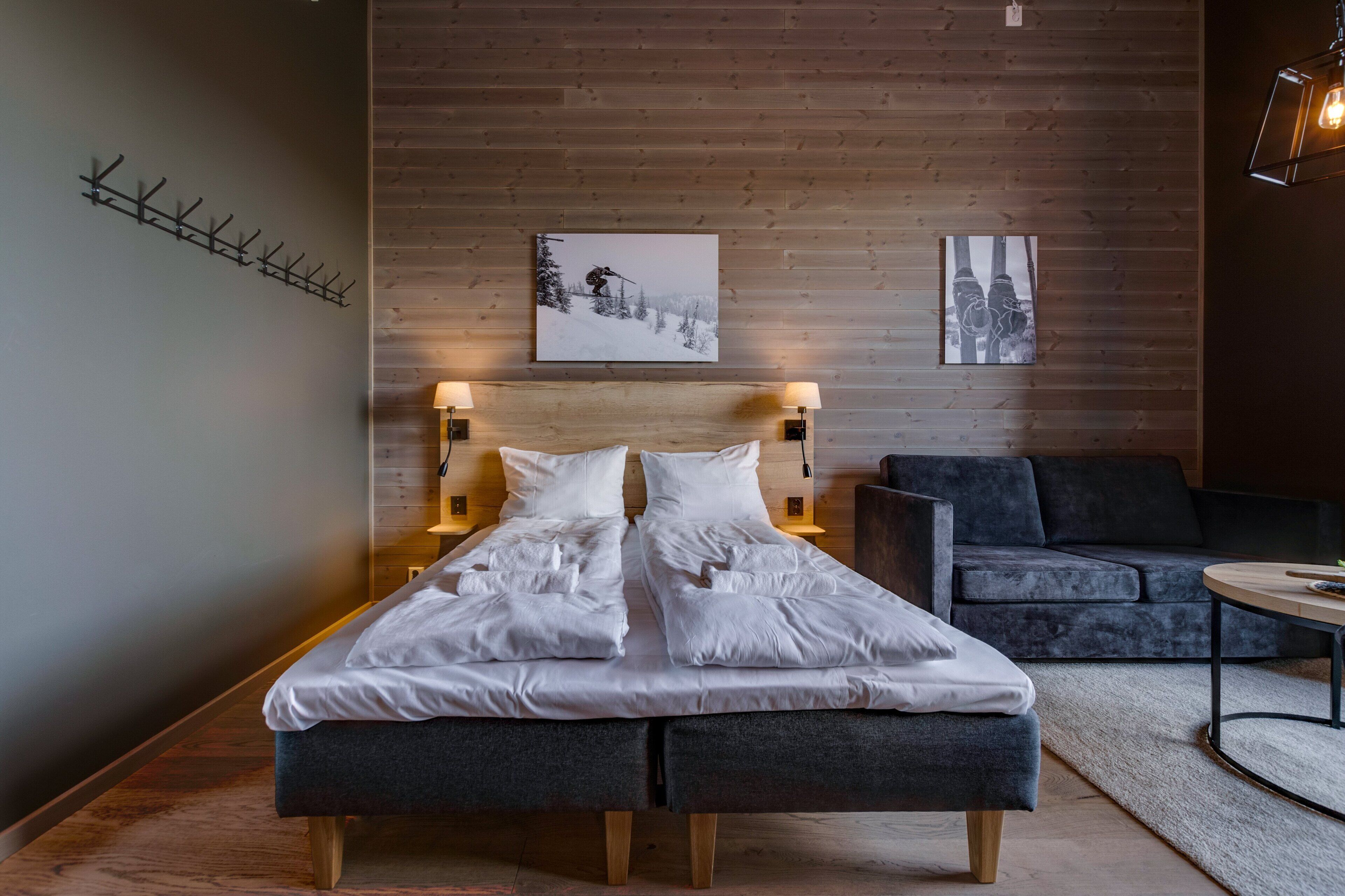 Une chambre moderne avec une tête de lit en bois, deux tables de chevet avec des lampes, un canapé gris et une petite table ronde.