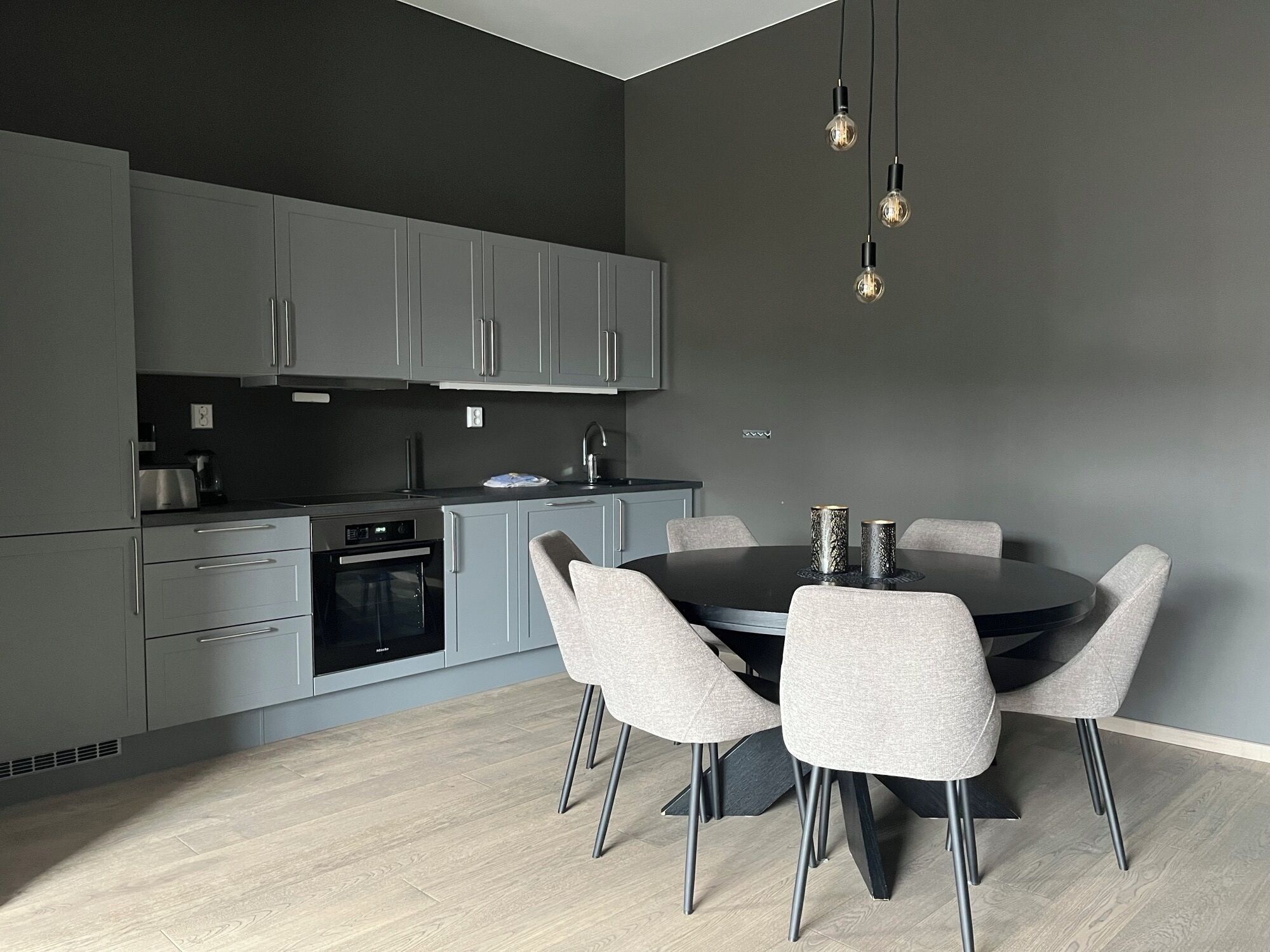 A modern kitchen with grey cabinets, a black countertop, and a round dining table with four chairs.