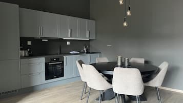 A modern kitchen with grey cabinets, a black countertop, and a round dining table with four chairs.