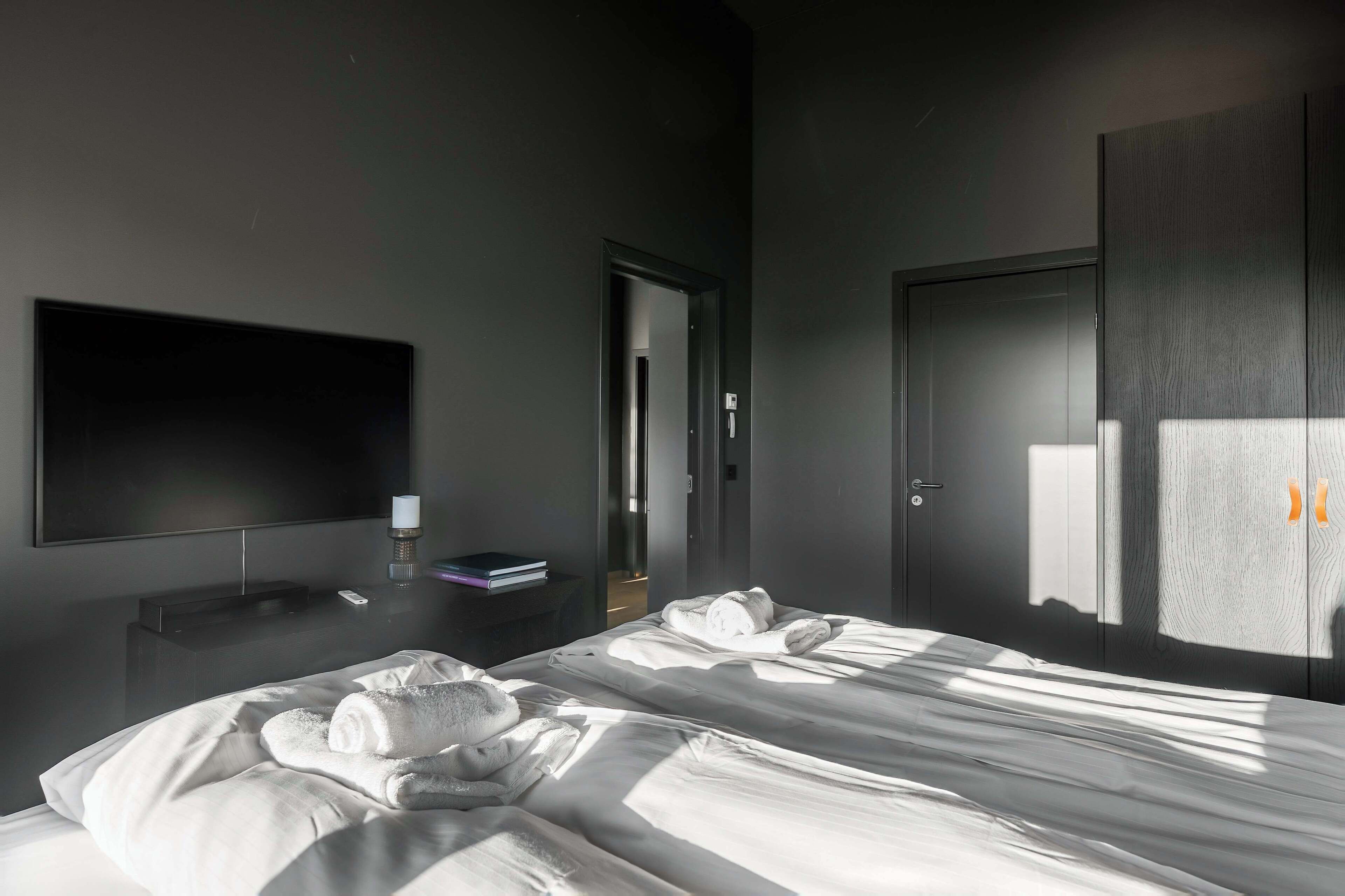 A modern hotel room with a bed, a flat-screen TV, a bedside table, and a wardrobe.
