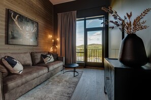 A modern living room with a leather sofa, a round coffee table, a large window with a view, and a vase with dried plants.