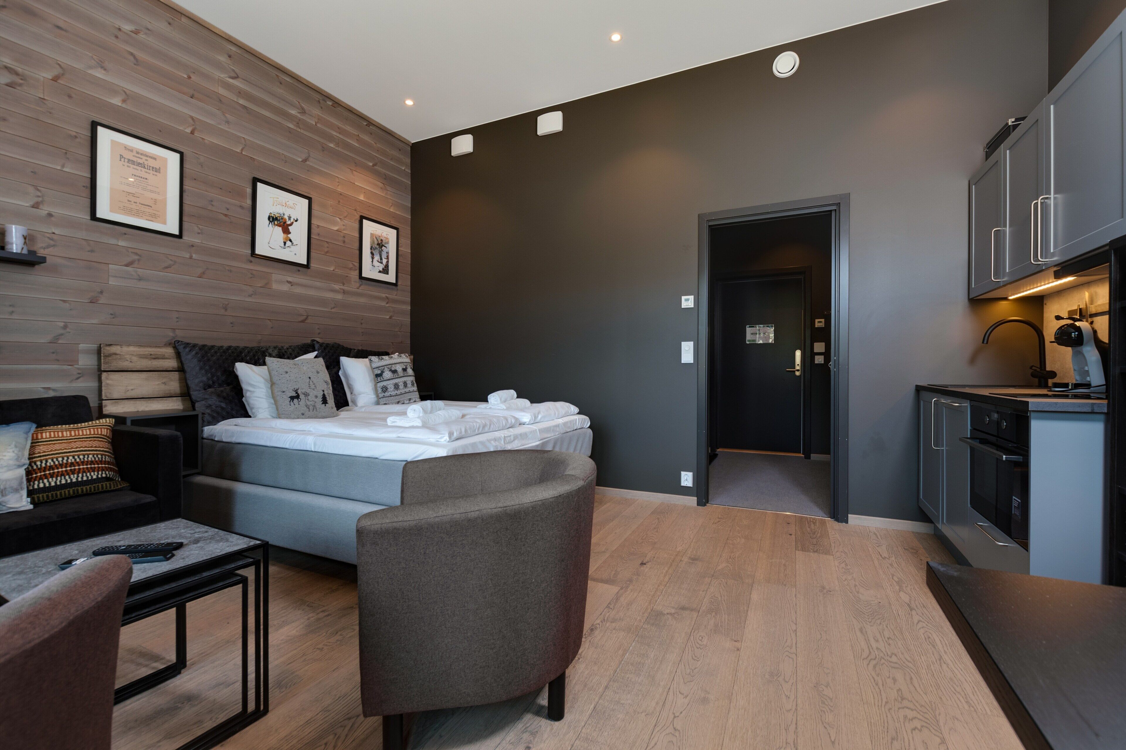 A modern bedroom with a bed, a sofa, a small table, and a kitchen area with cabinets and a countertop.