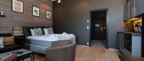 A modern bedroom with a bed, a sofa, a small table, and a kitchen area with cabinets and a countertop.