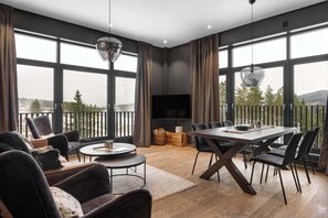 A modern living room with a large window, a dining area, and a flat-screen TV.