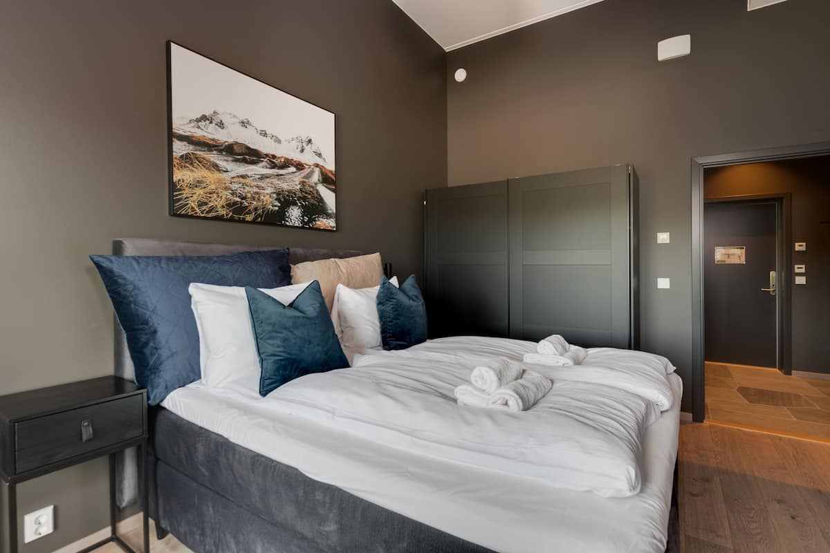 A modern bedroom with a large bed, dark walls, a framed picture, and a wardrobe.