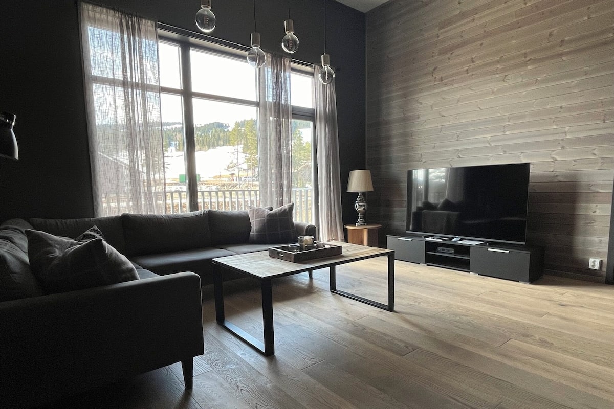 A modern living room with a sofa, coffee table, TV, and wooden flooring.