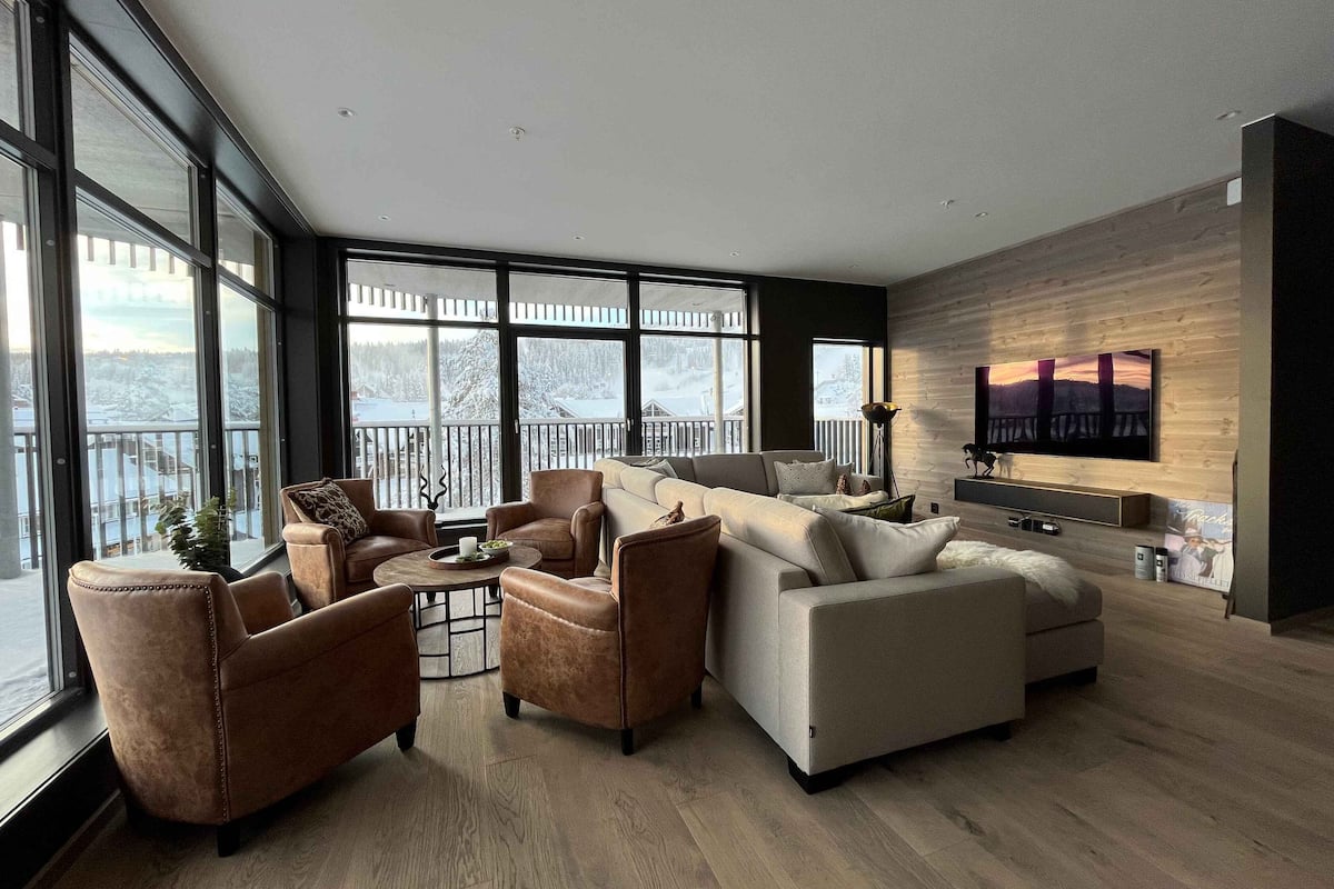 A modern living room with a large sectional sofa, armchairs, and a coffee table. There is a large window with a view of a snowy landscape.
