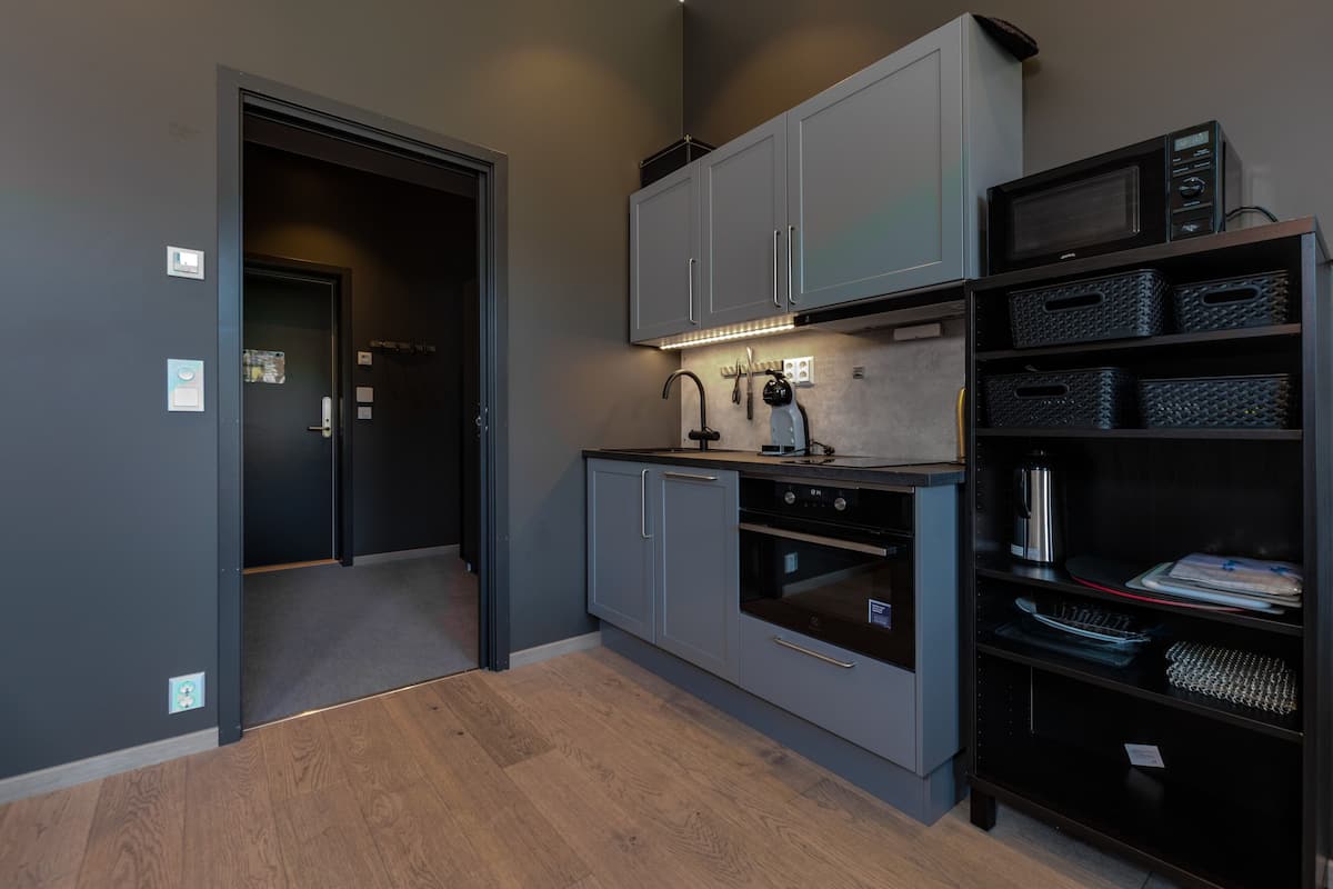 A compact kitchen with grey cabinets, a microwave, and a built-in oven.