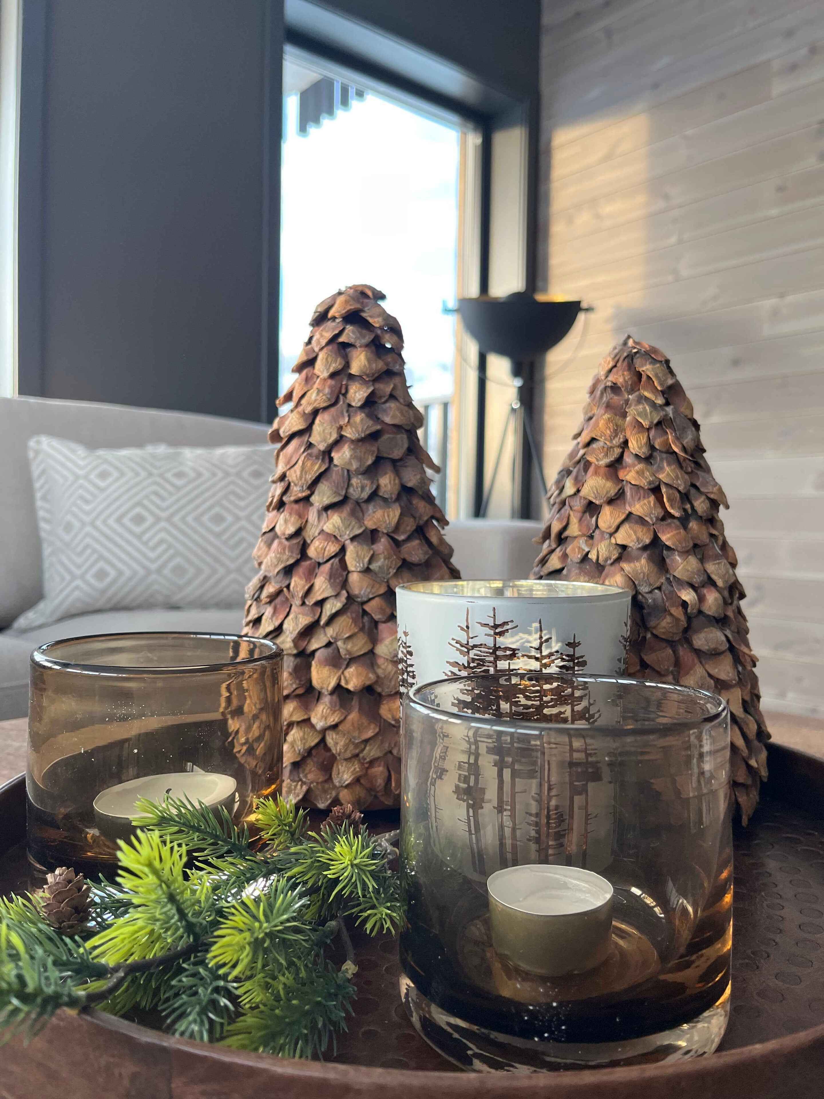 Una sala de estar moderna con una mesa de centro de vidrio que sostiene piñas decorativas y un candelabro de vidrio con una escena de un árbol en miniatura.