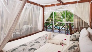 Ein Schlafzimmer mit Bett, Fenster mit Blick auf Pool und Palmen sowie einem Moskitonetz.