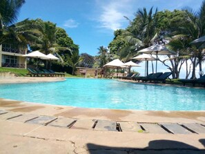 A swimming pool with lounge chairs and umbrellas, surrounded by palm trees and a clear sky. - Coral Beach Resort (Diani Beach)