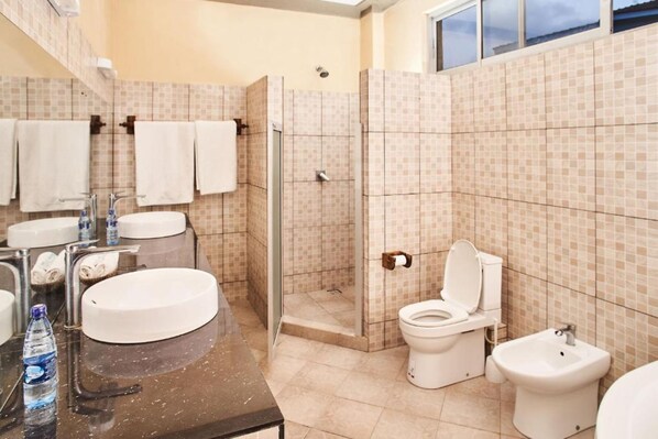 A bathroom with a large sink, a toilet, a bidet, and a shower area. - Coral Beach Resort (Diani Beach)