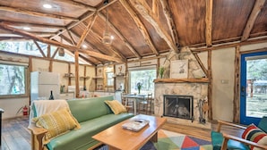 A rustic cabin interior with a green sofa, wooden coffee table, and a fireplace. - Unique Stay: Historic Home Along Blanco River (Blanco)