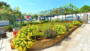 A garden with yellow flowers, a metal pergola, and parked cars in the background. - Apartment 1779/53709 (Istria - Banjole), 550m from the beach (Banjole)