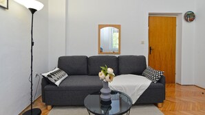 A living room with a grey sofa, a glass coffee table, a floor lamp, and a wooden door. - Apartment 1779/53709 (Istria - Banjole), 550m from the beach (Banjole)