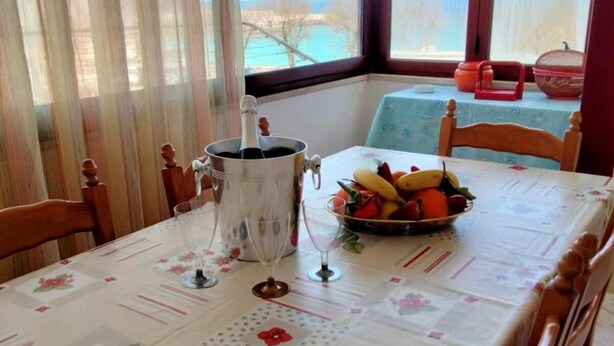 Et spisebord dækket med et blomstret dug, en skål med frugt, et vinglas og en champagneflaske.