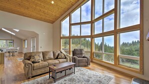A spacious living room with a large window, a wooden ceiling, a leather sofa, a recliner, and a coffee table. - Idyllic Retreat ~ 20 Mi to Olympic National Park! (Port Angeles)
