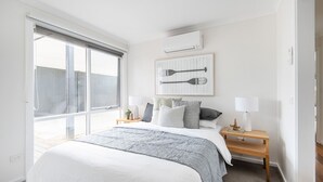 Un dormitorio con una cama grande, una ventana con vistas, aire acondicionado de pared y un cuadro enmarcado sobre la cama.