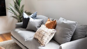 Un divano grigio con numerosi cuscini, una coperta tessuta e una pianta in vaso in un soggiorno.