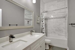 A bathroom with a double sink vanity, a large mirror, a shower with a glass door, and a tiled floor. - Cozy and Elegant 4 BR Home Perfect for Getaways (Indianapolis)