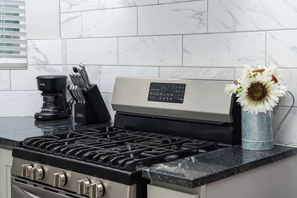 A kitchen with a gas stove, a coffee maker, and a flower vase.