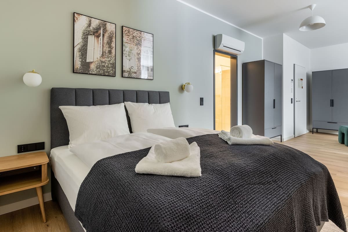 A modern hotel room with a large bed, two wall-mounted artworks, a bedside table, a bench, and a wardrobe.