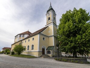 Une église dotée d’un clocher, une rue pavée et un grand arbre à l’avant.