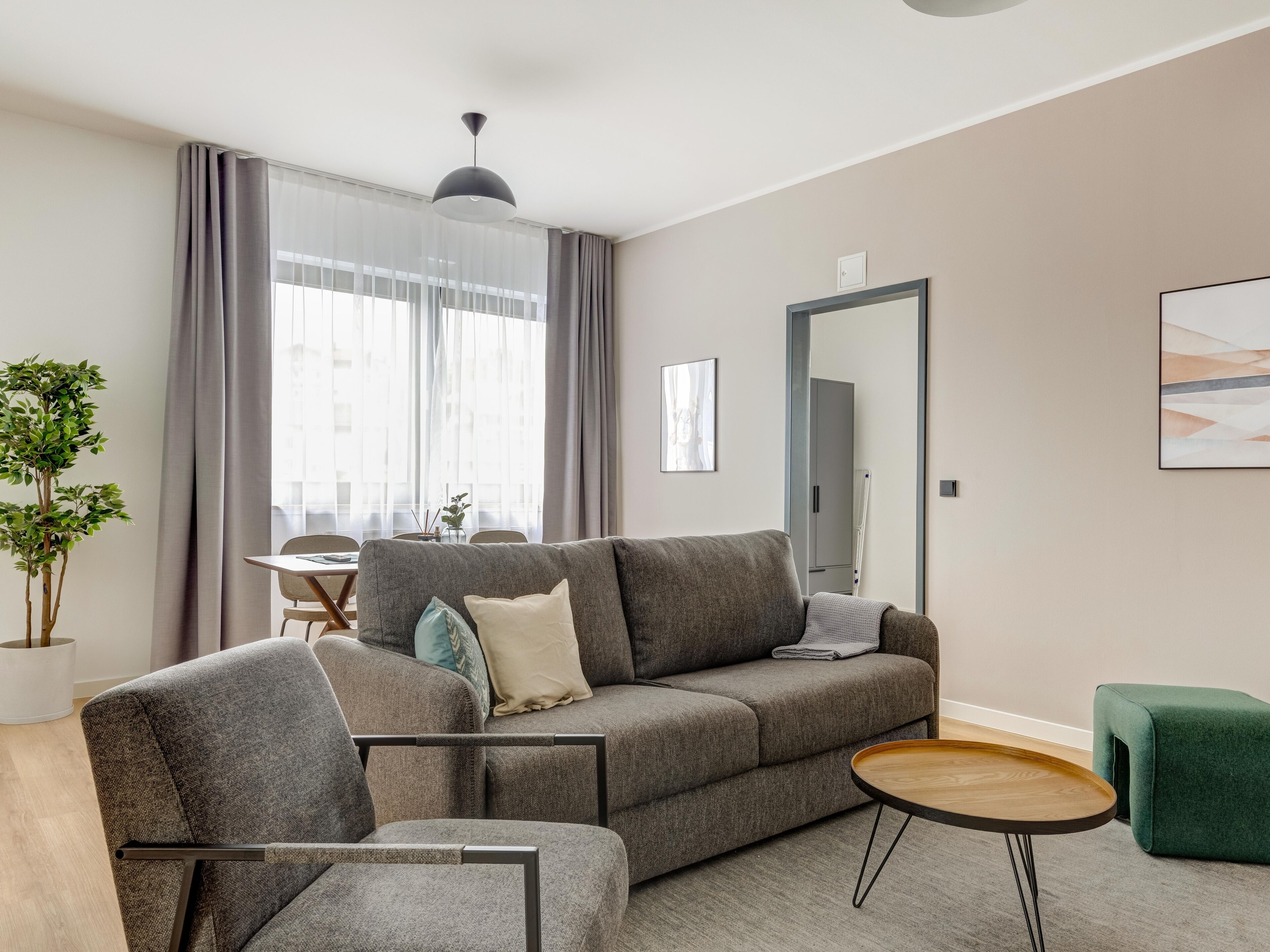 A modern living room with a grey sofa, a small round wooden table, and a green ottoman.