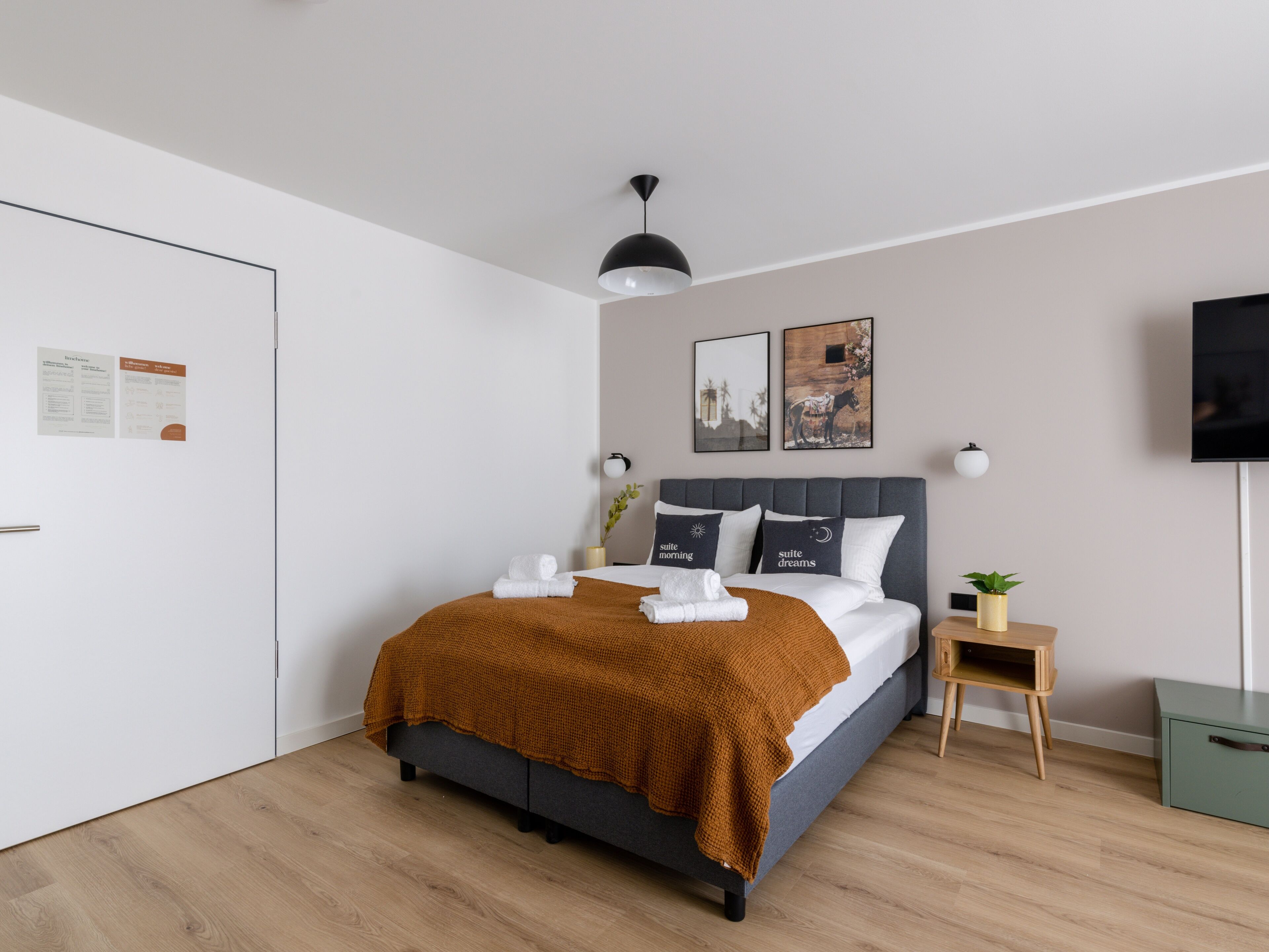 A modern bedroom with a bed, a bedside table, a TV, and a wall-mounted shelf.