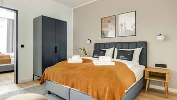 A modern bedroom with a large bed, a dark wardrobe, and a small bedside table.