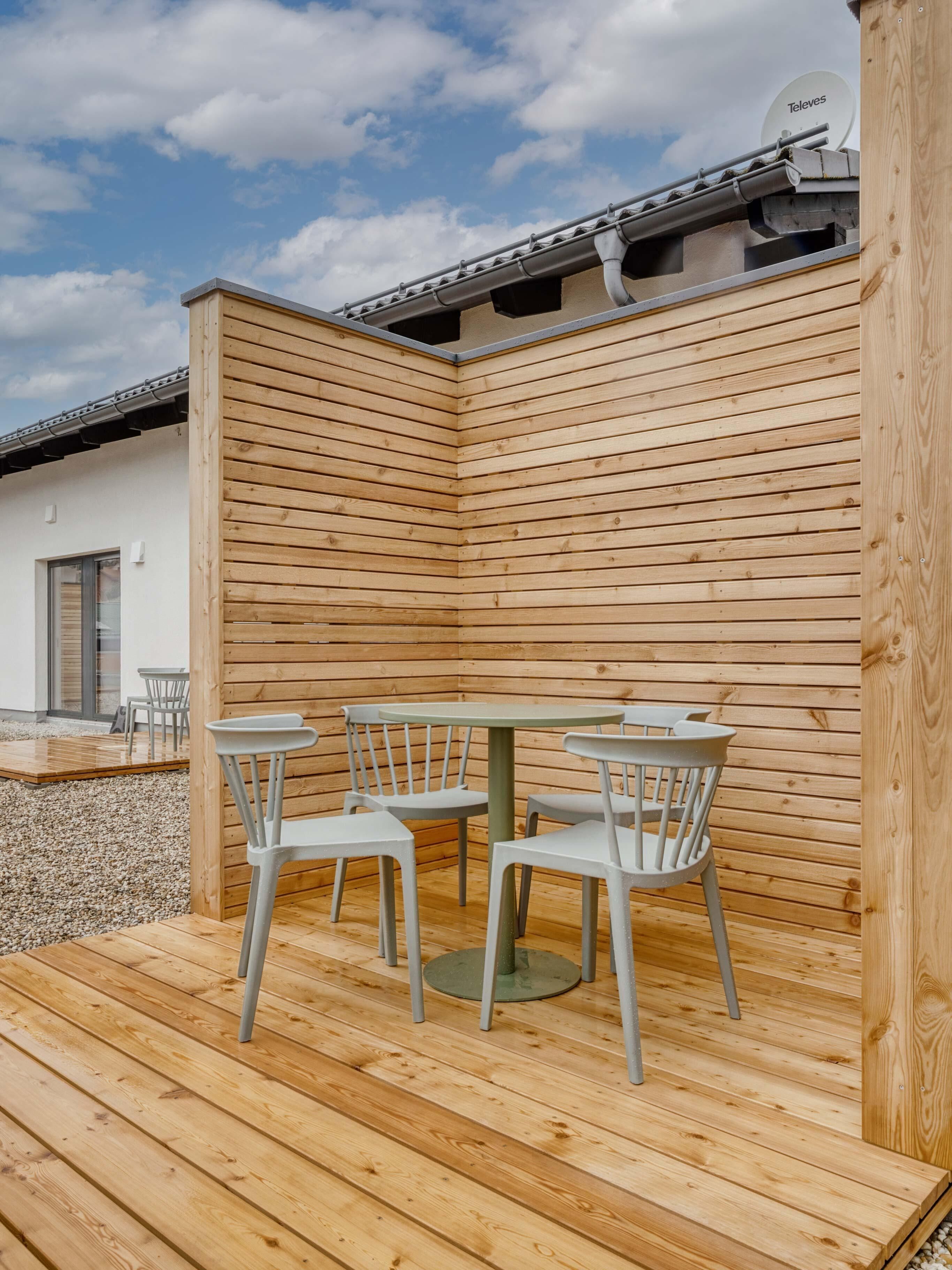 A wooden deck with a table and chairs, a satellite dish, and a building in the background.