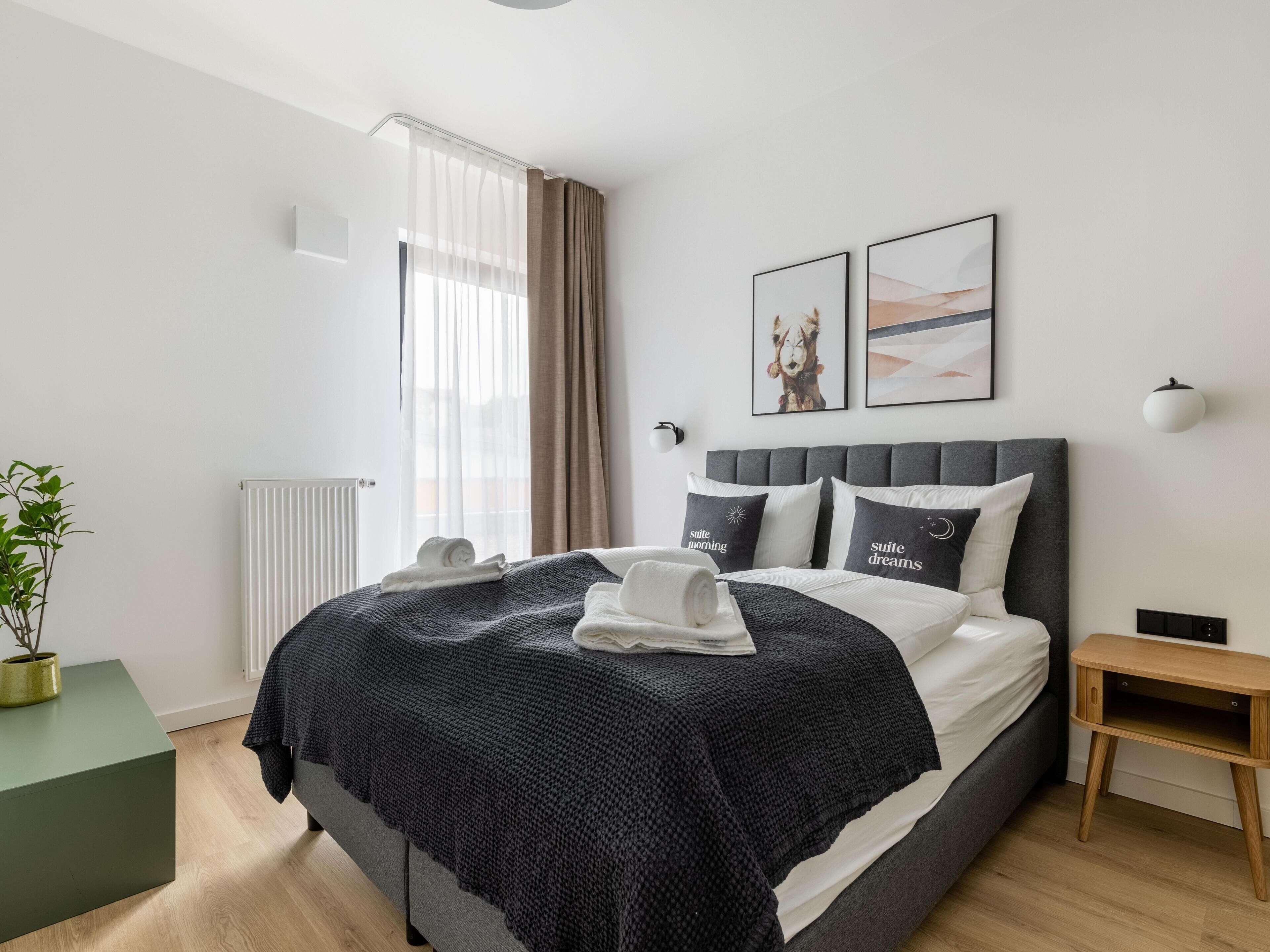 Een moderne hotelkamer met een groot bed, nachtkastje, een potplant en kunst aan de muur.