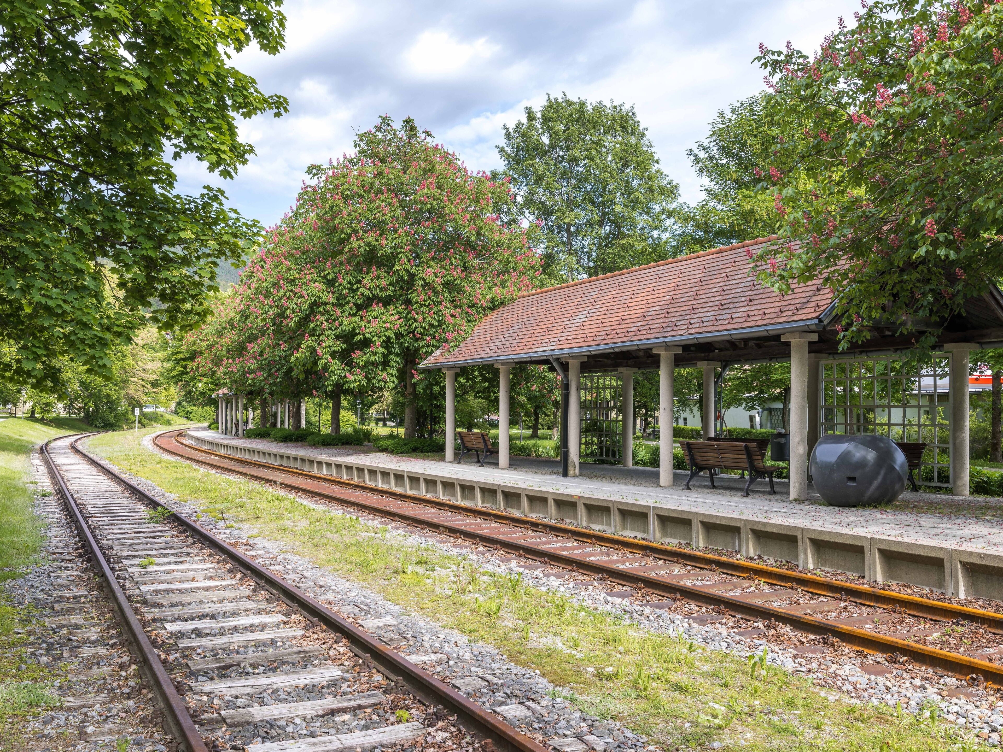A train station with a covered waiting area, benches, and a large sculpture.