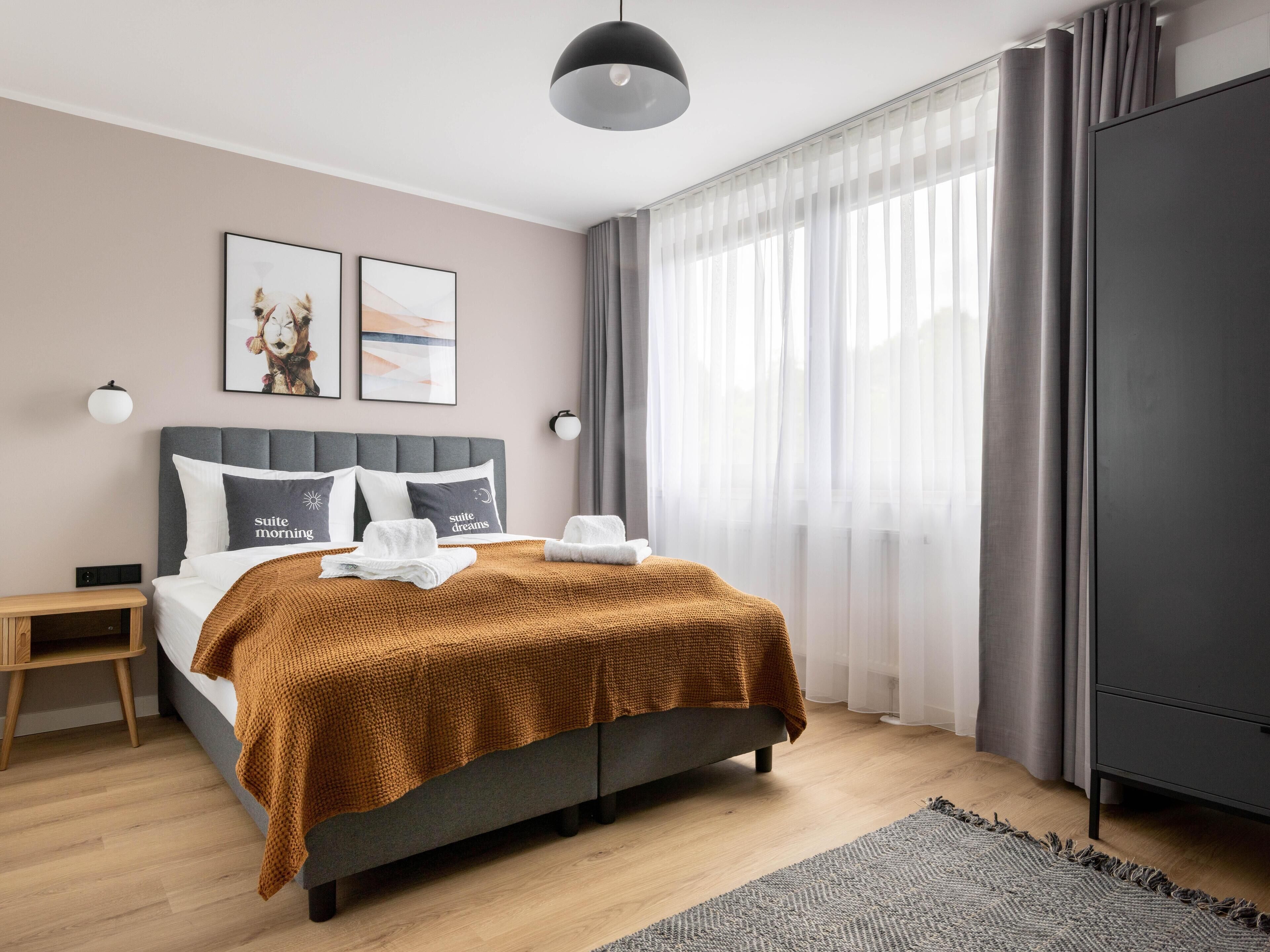 A modern bedroom with a bed, bedside tables, a wardrobe, and a large window with curtains.