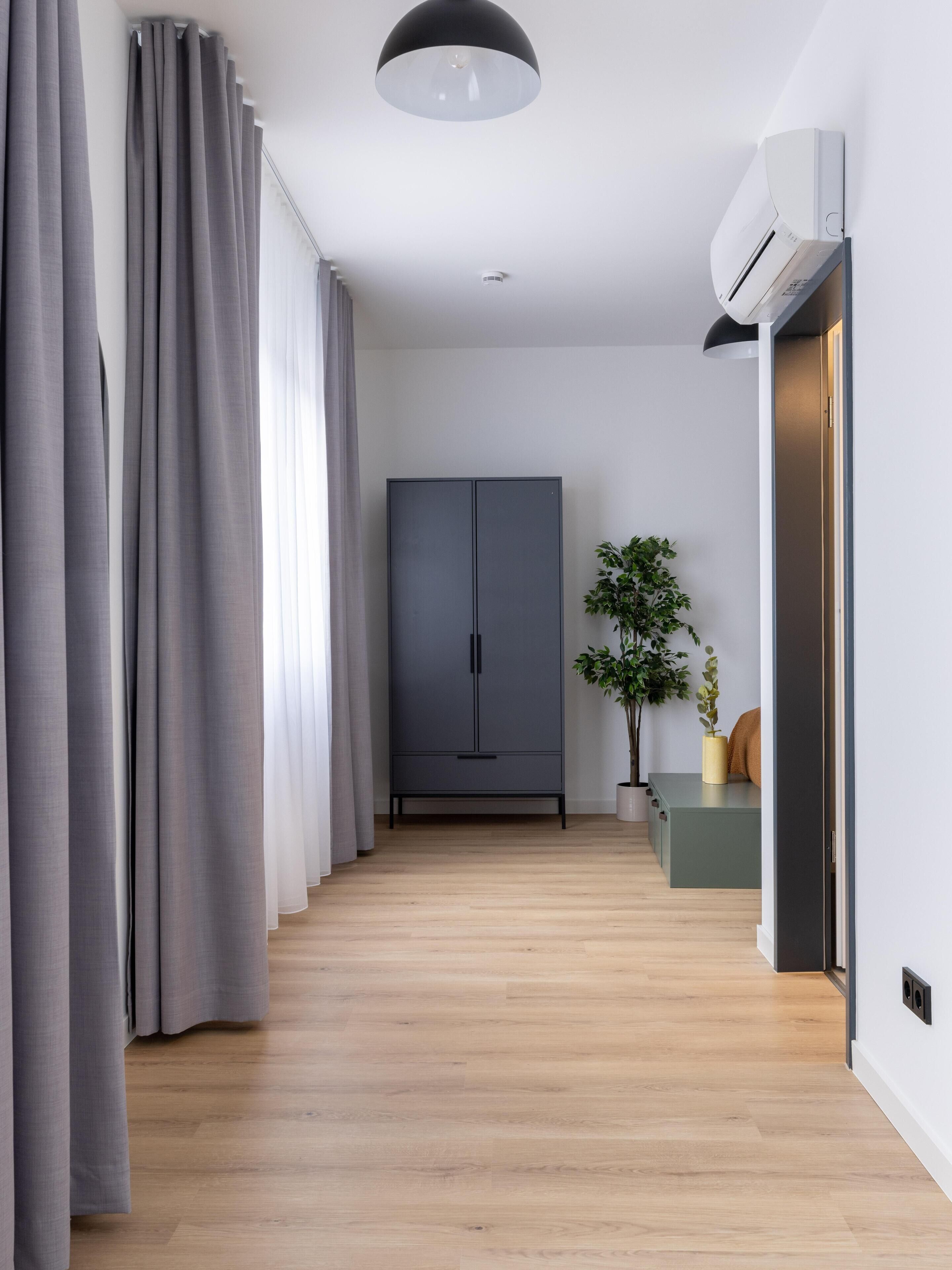 A modern hallway with grey curtains, a grey wardrobe, a potted plant, and a wall-mounted air conditioning unit.