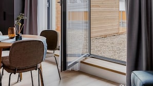 A modern living room with a dining area, large sliding glass doors leading to a balcony, and a view of buildings outside.