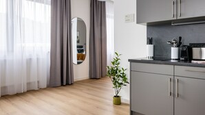 A modern kitchen with grey cabinets, a black pendant light, and a small potted plant.