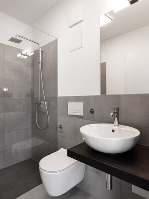 Une salle de bain moderne avec une douche à parois de verre, des toilettes blanches et un meuble-lavabo en bois foncé doté d’un évier blanc.