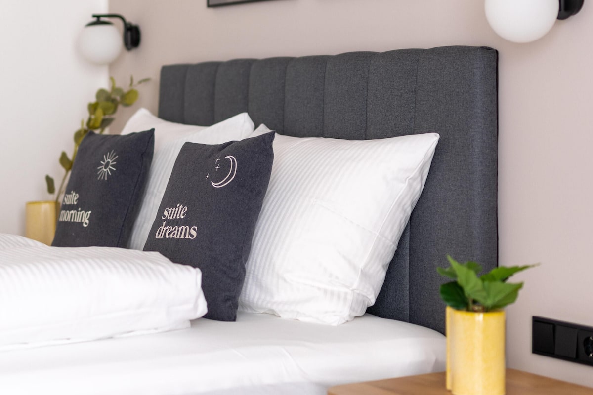 A modern bedroom with a grey headboard, white bedding, and two framed pictures on the wall.