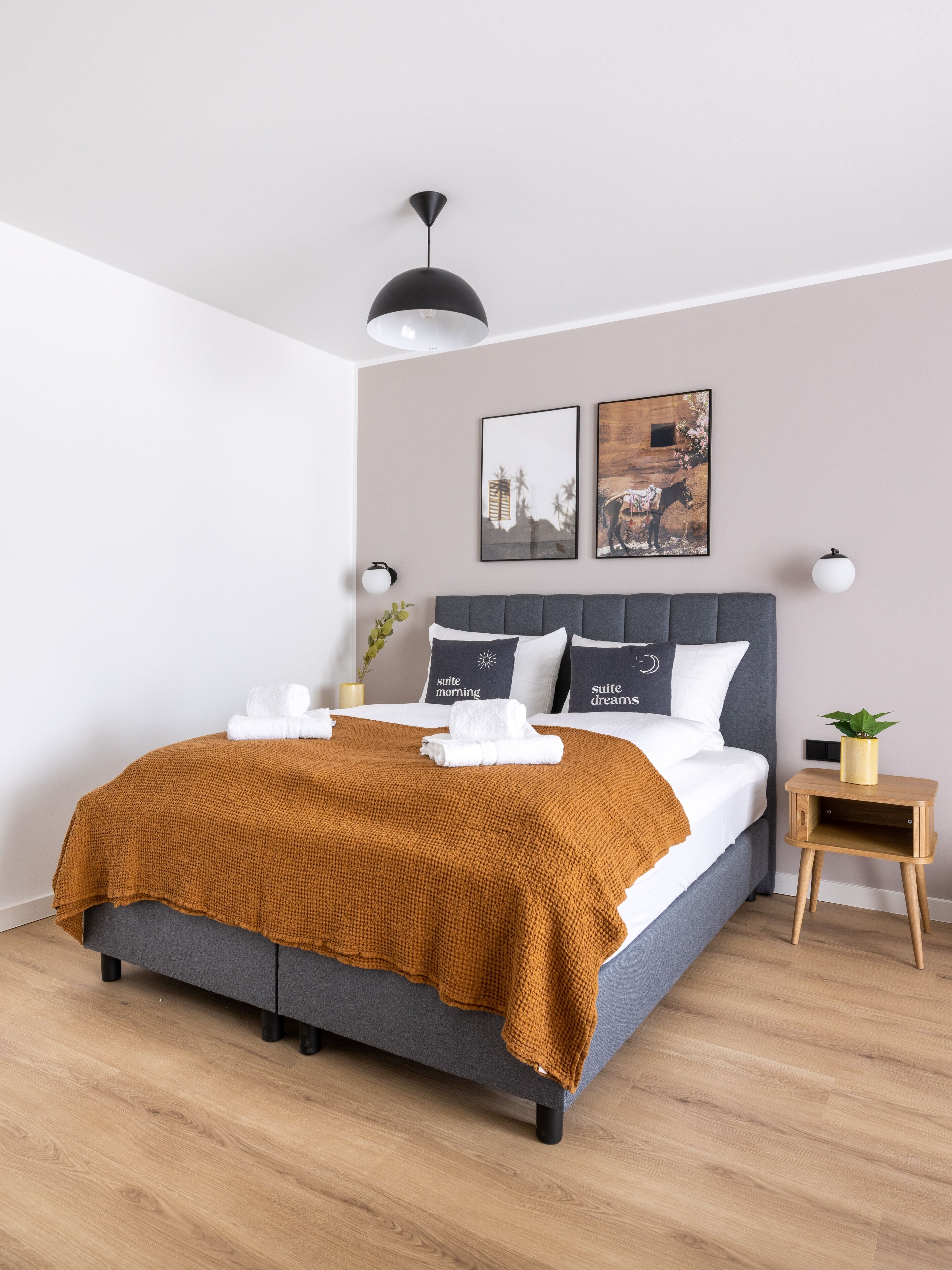 Ein modernes Schlafzimmer mit einem grau gepolsterten Bett, einer senffarbenen Decke und zwei Wandleuchten.