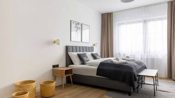 Een moderne slaapkamer met een bed, nachtkastjes, een klein bureau en een raam met dunne gordijnen.