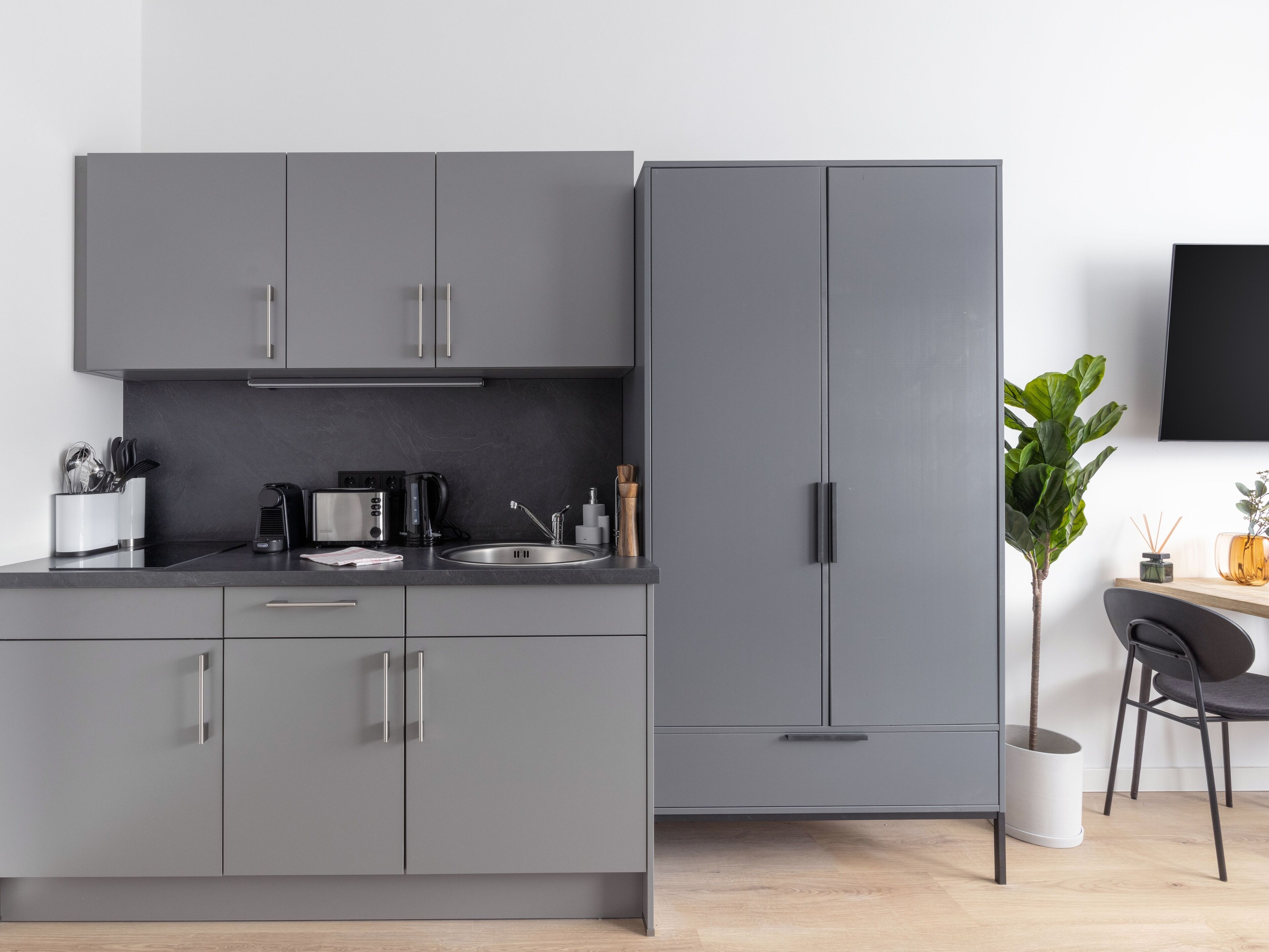Eine moderne Küche mit grauen Schränken, einer schwarzen Arbeitsplatte und einer Kaffeemaschine.