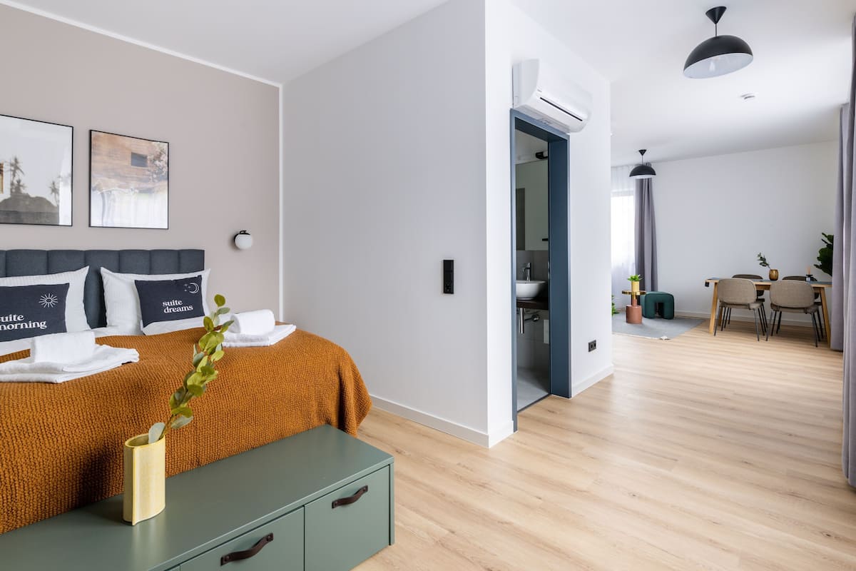 A modern hotel room with a bed, bedside table, and a view into the dining area.