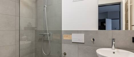 A modern bathroom with a glass-enclosed shower, a white toilet, and a large sink with a marble countertop.