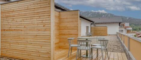 A wooden deck with a table and chairs, a covered seating area, and a view of a mountain in the background.