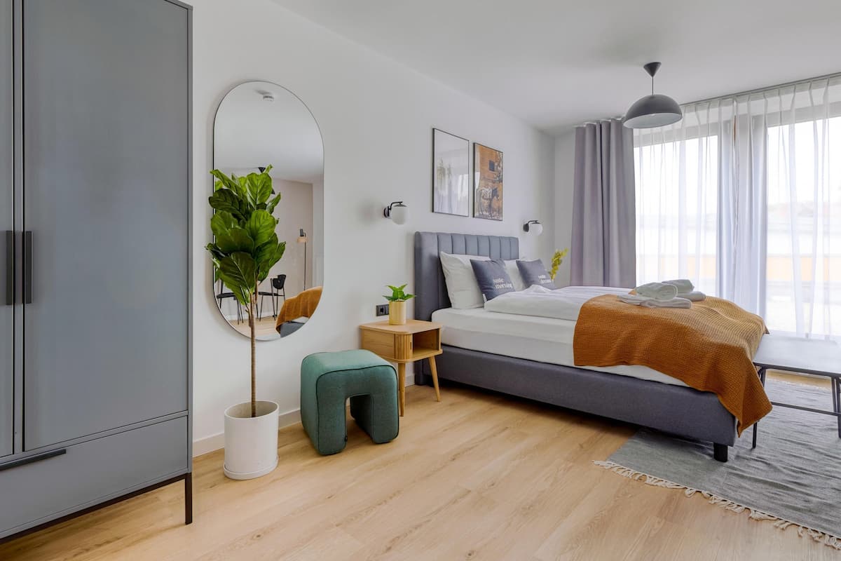 A modern bedroom with a bed, a wardrobe, a mirror, a small table, and a potted plant.