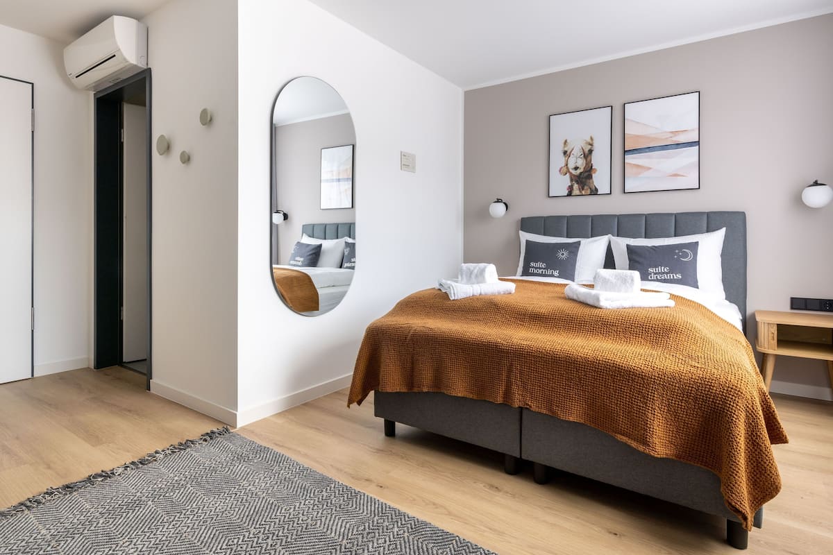 A modern hotel room with a bed, a round mirror, a bedside table, and a wall-mounted air conditioner.