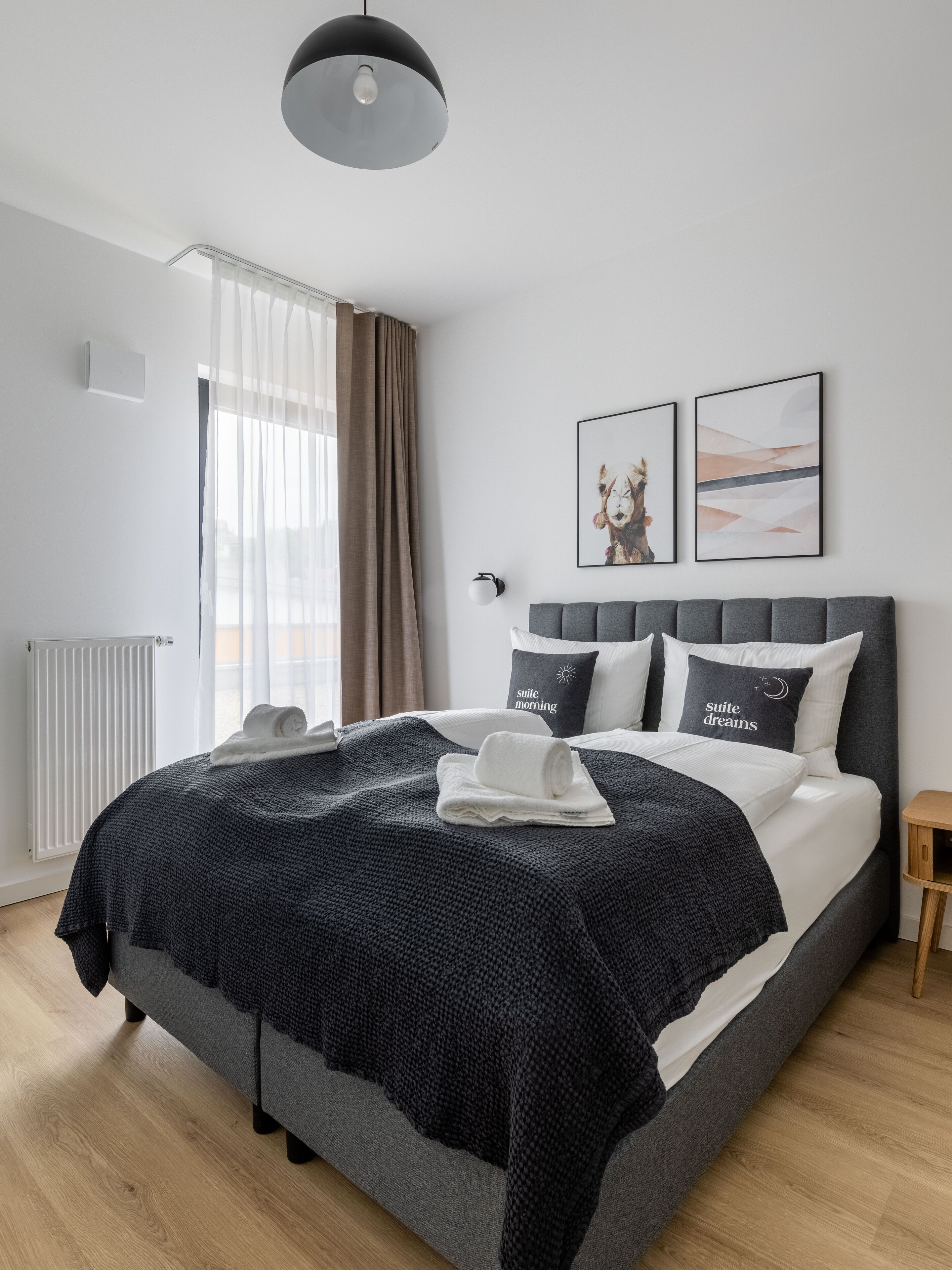 A modern bedroom with a large bed, a bedside table, a radiator, and a window with curtains.