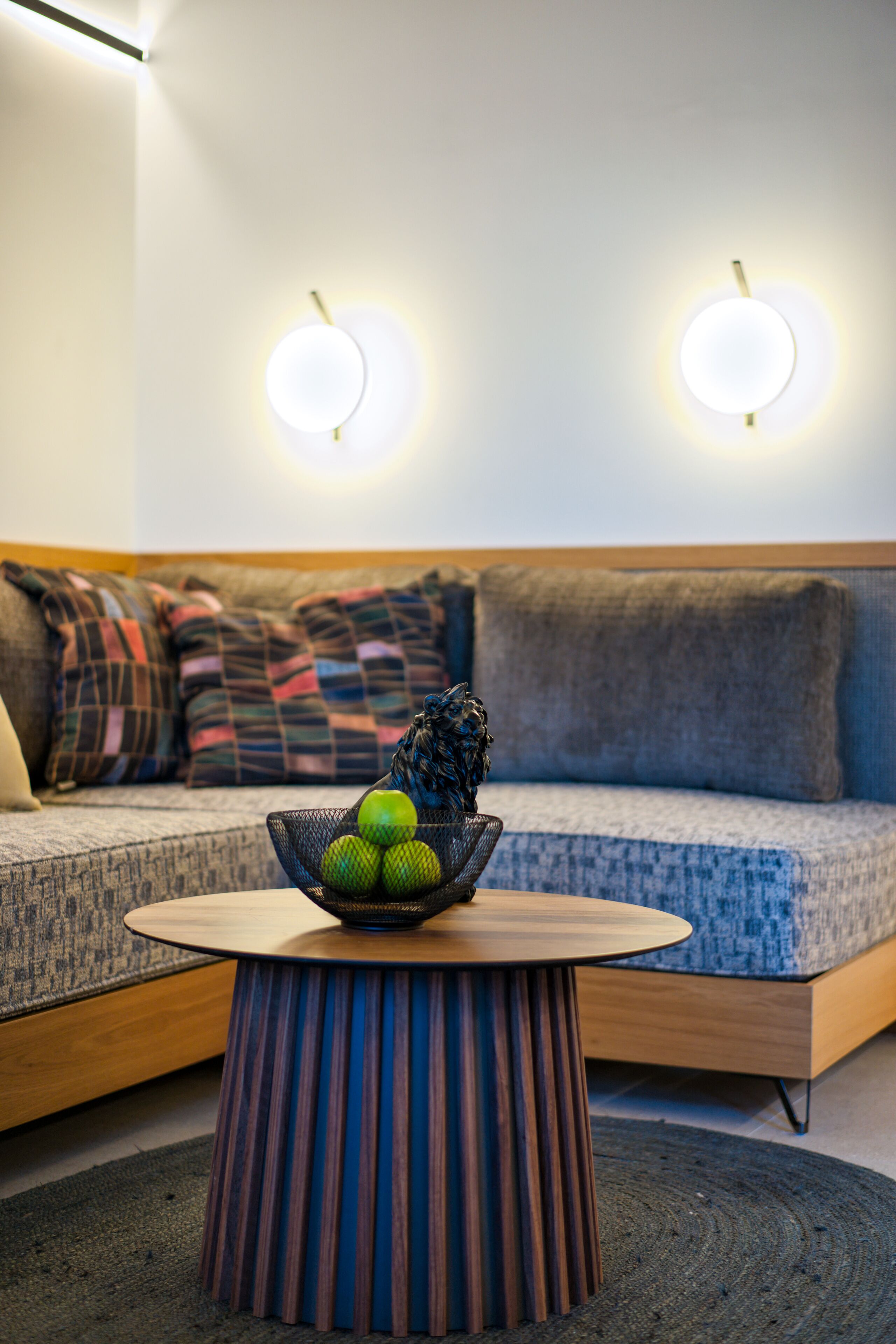 Ein modernes Wohnzimmer mit einem runden Couchtisch, einer Obstschale und einem Sofa mit gemusterten Kissen.