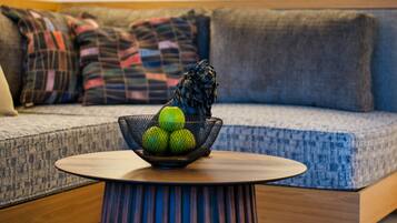 Ein modernes Wohnzimmer mit einem runden Couchtisch, einer Obstschale und einem Sofa mit gemusterten Kissen.